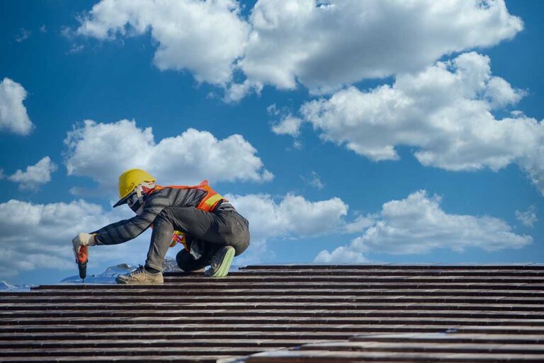 A roofer applies a light-colored coating across a clean low-slope roof beside sealed seams and drainage areas.